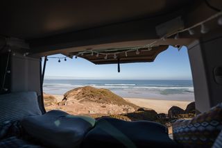 Aus der Heckklappe eines Campers, der am Strand steht, sieht man das Meer beim Überwintern in Portugal.