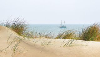 Dünenlandschaft mit einem Schiff im Hintergrund