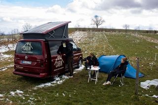 Roter Campervan mit 3 Personen die campen