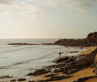 Frau steht am Strand und schaut aufs Meer