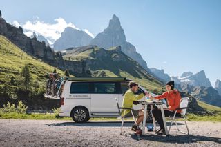 Zwei Personen beim Frühstück vor dem Camper vor einem Bergpanorama