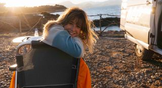 Woman laughing on camping chair next to off camper at sunset