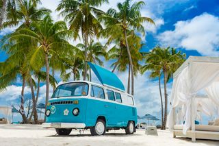 Blauer VW Bulli an Strand mit Palmen und Surfboards