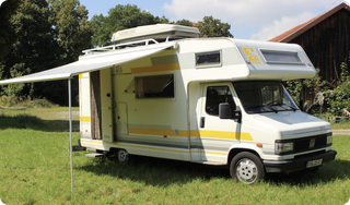 Paul und Andis altes Wohnmobil "Woody" steht auf einer Wiese.