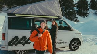 Junge Frau mit orangefarbener Jacke beim Wintercamping im Schnee