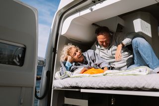 Ein Urlaub im April: Ein Paar liegt nebeneinander im Camper in der Sonne und lacht herzlich